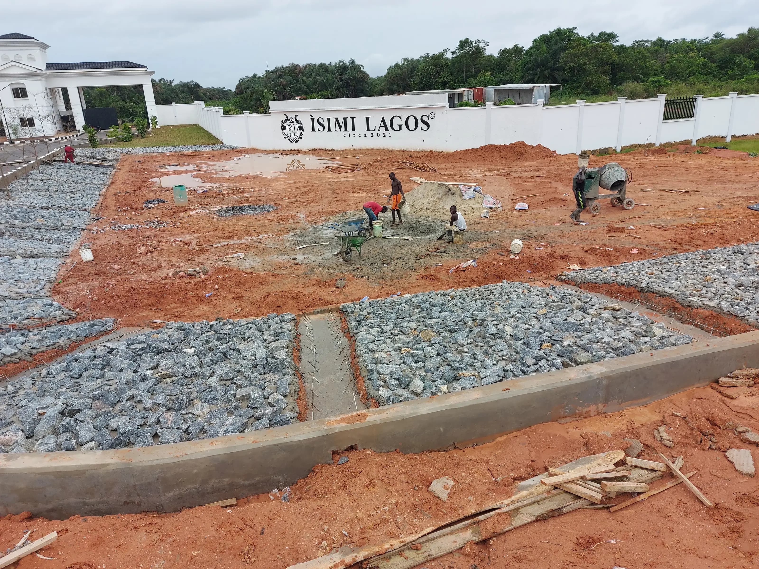 Site workers mixing concrete in front of the Isimi Lagos estate wall, with kerbstone and drainage works underway